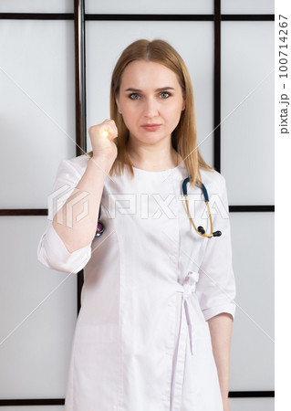Portrait of a female doctor in a white uniform with a glowing flashlight in her hand and a stethoscope around her neck 100714267