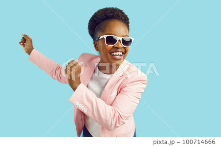 Dancing laughing african american woman in pink jacket and sunglasses on turquoise background. 100714666