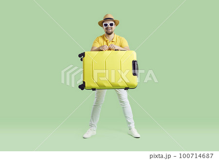 Happy cheerful man in summer hat and sunglasses holding his holiday luggage and laughing 100714687