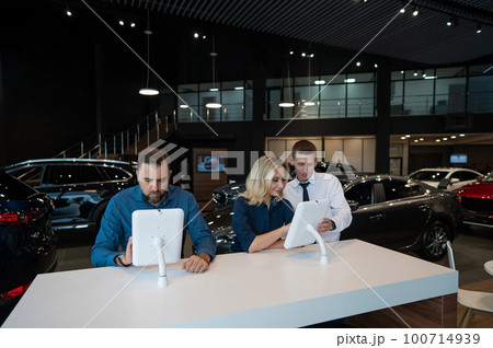 Caucasian married couple chooses a car in a car dealership on digital tablets. Caucasian married couple chooses a car in a car dealership on digital tablets. 100714939