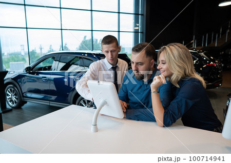 Caucasian married couple chooses a car in a car dealership on digital tablets. Caucasian married couple chooses a car in a car dealership on digital tablets. 100714941