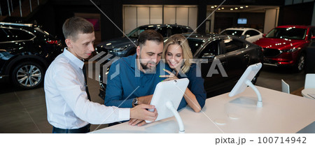 Caucasian married couple chooses a car in a car dealership on digital tablets. Caucasian married couple chooses a car in a car dealership on digital tablets. 100714942
