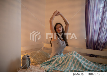 A woman stretches sitting on her bed in the bedroom. A woman stretches sitting on her bed in the bedroom. 100715209