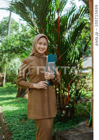 asian female teacher in hijab carrying clipboard and a tablet asian female teacher in hijab carrying clipboard and a tablet 100715699