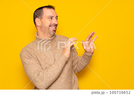 Bearded hispanic man in a turtleneck ducking to the side in embarrassment, tries to push away from something or someone with his hands. Isolated on yellow background. 100716652
