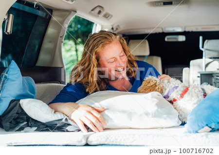 Laughing middle-aged woman having fun with cockapoo puppy pet while lying in camper car vehicle during road trip. Window view. Best friend. Enjoying free lifestyle, travel, vacation, freedom. Laughing middle-aged woman having fun with cockapoo puppy pet while lying in camper car vehicle during road trip. Window view. Best friend. Enjoying free lifestyle, travel, vacation, freedom. 100716702