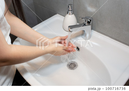 Young beautiful woman washes her hands with soap in the bathroom, toilet. Regular hand washing for hygiene. 100716736