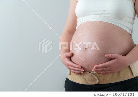 Pregnant woman putting on supporting bandage to reduce backache