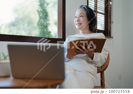 Portrait of an elderly Asian woman in a modern pose holding a memory notebook and operating a computer Portrait of an elderly Asian woman in a modern pose holding a memory notebook and operating a computer 100723558