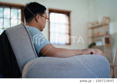 Portrait of a man with glasses suffering from depression sitting on the sofa 100723645