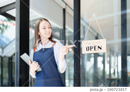 Starting and opening a small business, a young Asian woman showing a smiling face in an apron standing in front of a coffee shop bar counter. Business Owner, Restaurant, Barista, Cafe, Online SME. Starting and opening a small business, a young Asian woman showing a smiling face in an apron standing in front of a coffee shop bar counter. Business Owner, Restaurant, Barista, Cafe, Online SME. 100723857