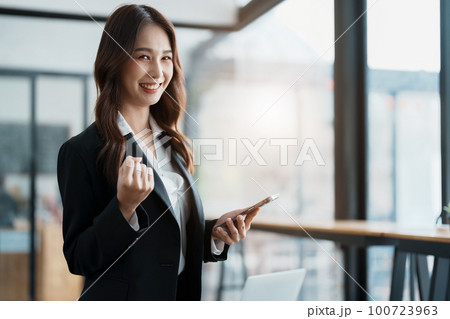 Business work concept, portrait of a young businesswoman holding a cell phone showing a happy expression, business success 100723963