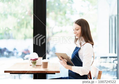 Starting and opening a small business, a young Asian woman showing a smiling face in an apron standing in front of a coffee shop bar counter. Business Owner, Restaurant, Barista, Cafe, Online SME. 100724522