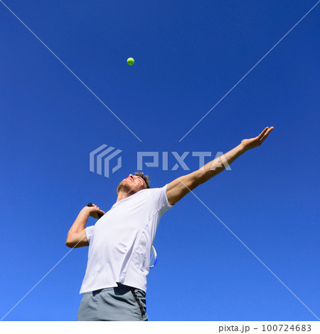 Tennis player man doing serve in position to hit ball in the air. Playing tennis outdoors on blue sky summer background. Active sport athlete doing fitness fun. Tennis player man doing serve in position to hit ball in the air. Playing tennis outdoors on blue sky summer background. Active sport athlete doing fitness fun. 100724683