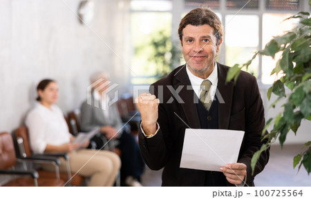 Happy man with papers making woohoo gesture in office 100725564