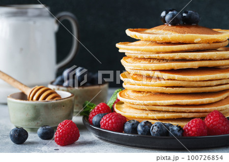 Delicious pancakes, with fresh blueberries, raspberry and maple syrup or honey on a dark background Delicious pancakes, with fresh blueberries, raspberry and maple syrup or honey on a dark background 100726854