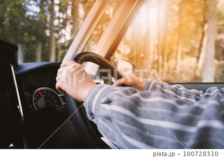 車のハンドルを握る運転手・道路での運転の手 100728310