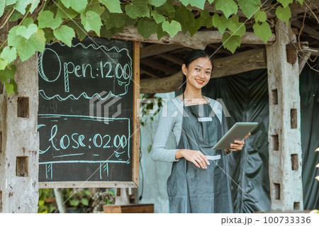 female barista using the digital tablet while standing outside the coffee shop female barista using the digital tablet while standing outside the coffee shop 100733336