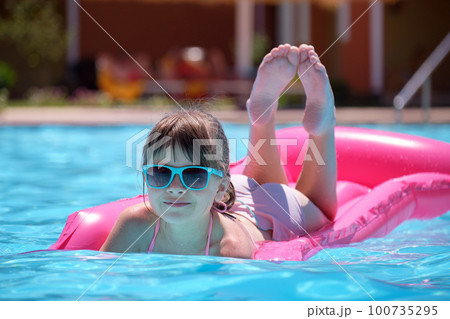 Young joyful child girl having fun swimming on inflatable air mattress in swimming pool with blue water on warm summer day on tropical vacations. Summertime activities concept 100735295