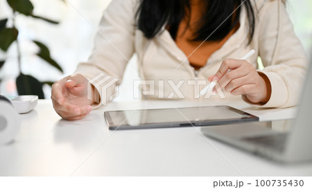 Cropped image of an Asian woman using her digital tablet at her desk. Cropped image of an Asian woman using her digital tablet at her desk. 100735430