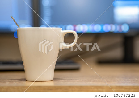 White cup of coffee or tea on blurred background of personal computer screen. White cup of coffee or tea on blurred background of personal computer screen. 100737223