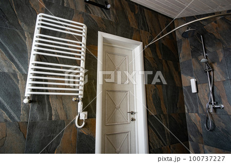 White contemporary electric towel dryer mounted on black tiled wall in modern bathroom. White contemporary electric towel dryer mounted on black tiled wall in modern bathroom. 100737227