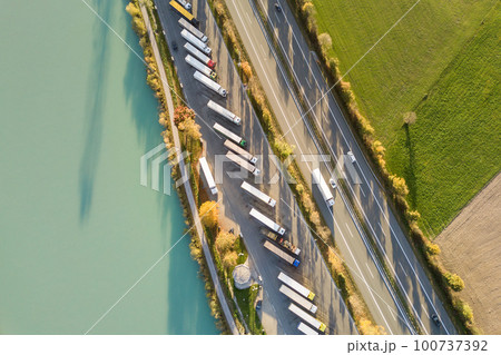 Top down aerial view of highway interstate road with fast moving traffic and parking lot with parked lorry trucks. Top down aerial view of highway interstate road with fast moving traffic and parking lot with parked lorry trucks. 100737392
