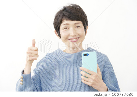 スマホを持ってグッドサインする中年女性 白背景 スマホを持ってグッドサインする中年女性 白背景 100737630