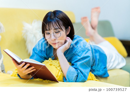 ソファーに寝転んで本を読む女性 100739527