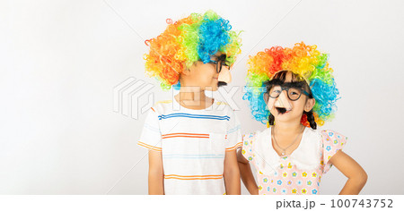 April Fool's Day. Two brothers funny kid boy and little girl clown wears curly wig colorful big nos and glasses and has mustache isolated on white background, Happy children festive decor 100743752