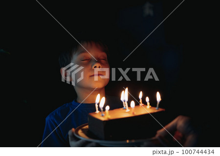 little cute caucasian boy making a wish before puffing out a candle on cake on his 6 birthday 100744434