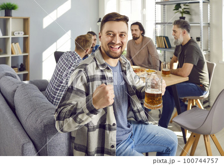 Happy young man is having fun and drinking beer at a home party with his friends 100744757