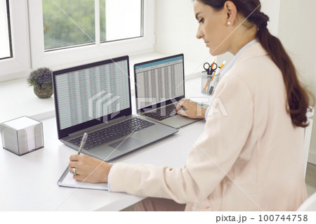 Young business woman accountant working on a laptop with tables at office. Young business woman accountant working on a laptop with tables at office. 100744758