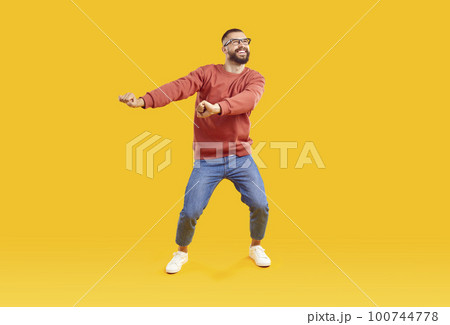 Cheerful and positive man in good mood having fun dancing on yellow background. 100744778