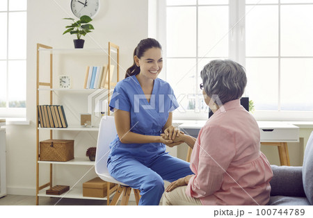 Happy friendly nurse or caregiver smiling and holding a senior woman by the hand 100744789