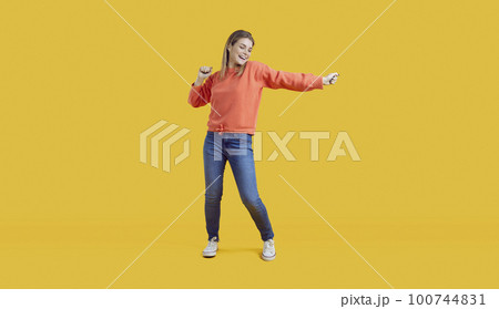 Happy young woman dancing on yellow background 100744831