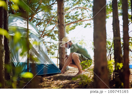 caucasian man wearing a hat putting up a tent. Family camping concept caucasian man wearing a hat putting up a tent. Family camping concept 100745165