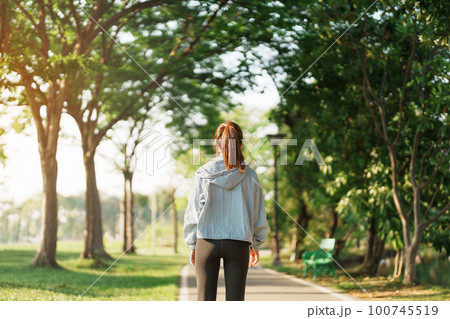 Young adult female in pink sportswear stretching muscle in the park outdoor, sport woman warm up ready for running and jogging in morning. wellness, fitness, exercise and work life balance concepts 100745519
