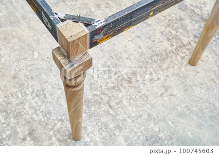 Wooden carved leg of solid oak with metal table frame during manufacturing process of dining table in workshop close up view Wooden carved leg of solid oak with metal table frame during manufacturing process of dining table in workshop close up view 100745603