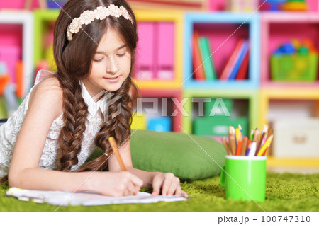 Beautiful little girl draws with a pencil on a sheet of paper  100747310