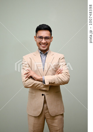Smart Asian businessman stands against a green studio background with arms crossed. 100748398