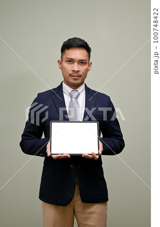 Thoughtful Asian businessman holding a tablet, showing tablet blank screen mockup to camera 100748422