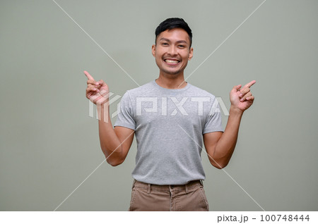 Smiling Asian man pointing his fingers up at the empty space. isolated background 100748444