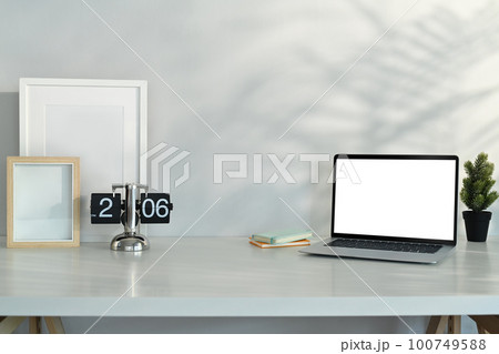 Laptop, vintage flip clock, blank picture frame and houseplant on white table. Copy space for your text 100749588