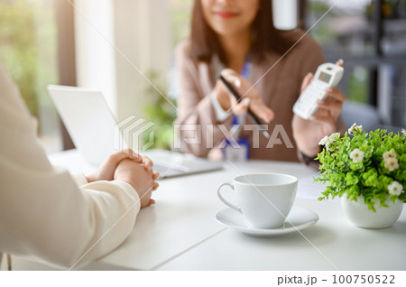 Cropped image of professional Asian female banker talking with a female client in the office. Cropped image of professional Asian female banker talking with a female client in the office. 100750522