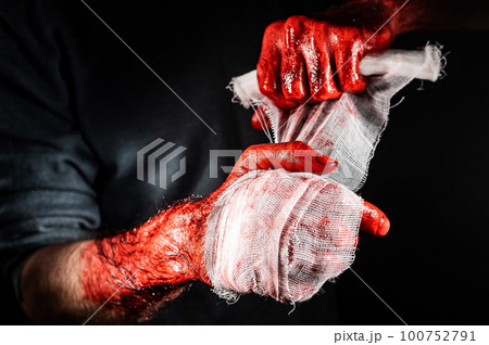 A man covered in blood bandages his hands. A man covered in blood bandages his hands. 100752791