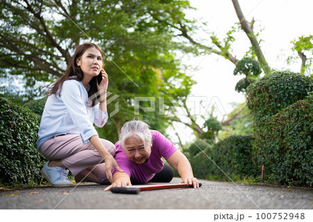 Asian senior woman fell down on lying floor because faint and limb weakness and pain from accident and woman came to help support and call emergency. Concept of old elderly insurance and health care Asian senior woman fell down on lying floor because faint and limb weakness and pain from accident and woman came to help support and call emergency. Concept of old elderly insurance and health care 100752948