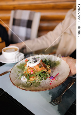Waiter bring breakfast for customer on terrace. Fresh sandwich with salmon and poached egg on top Waiter bring breakfast for customer on terrace. Fresh sandwich with salmon and poached egg on top 100754623