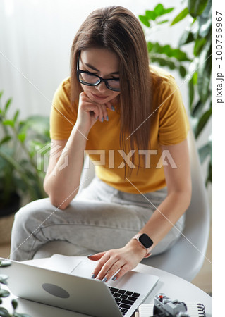 Young woman designer or freelancer working at home using computer sitting at table at home 100756967