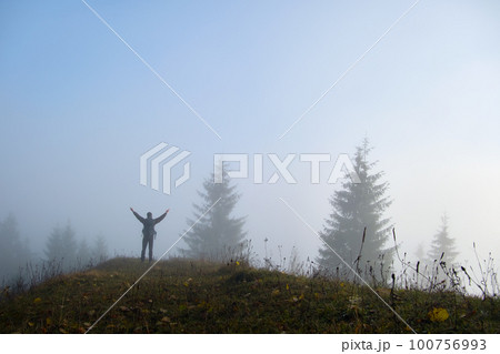 Small figure of lonely hiker enjoying his time on wild forest trail on foggy autumn day Small figure of lonely hiker enjoying his time on wild forest trail on foggy autumn day 100756993
